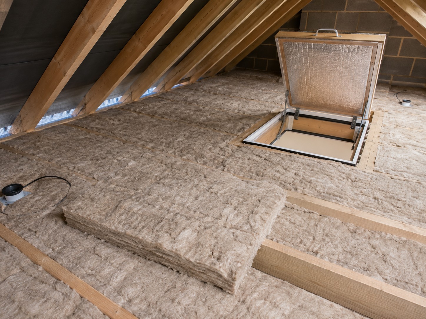 Mineral wool being laid across loft joists beside the hatch